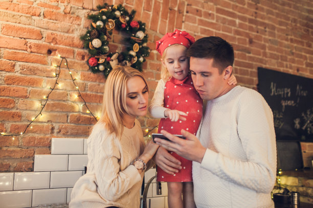 幸福的家庭——在一个阁楼式的厨房里，妈妈、爸爸和女儿正在用智能手机寻找圣诞饼干的配方图片下载