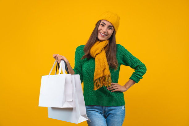 迷人的微笑自信的女孩肖像穿着舒适的针织衫和一堆购物袋孤立在黄色的背景图片下载