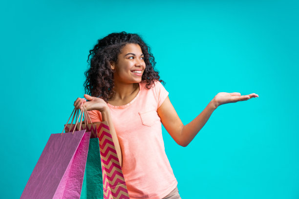 一幅迷人的微笑随意穿着的年轻女子的肖像，拿着一堆购物袋，用她的手掌指向一边图片下载