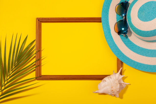 顶部视图条纹蓝色帽子，太阳镜，棕榈叶，贝壳和框架的假期照片在黄色的背景。海滩度假、海上旅游、温暖阳光夏日的概念。复制粘贴图片下载