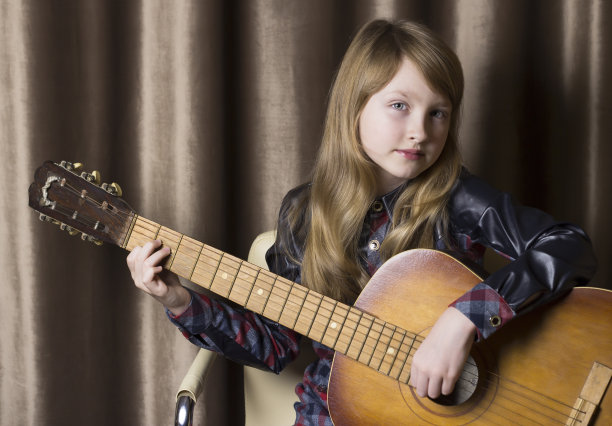 一个小女孩拿着吉他，背景是棕色的。图片下载