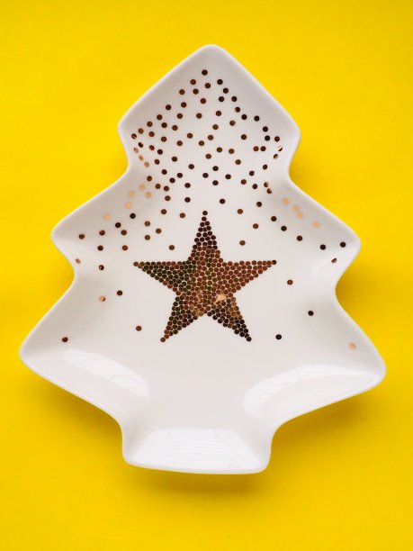 圣诞树形状的白色盘子，上面有金色的装饰，中间有一颗星星。黄色背景。新年或圣诞卡片。广告背景和祝贺。副本的空间。图片下载