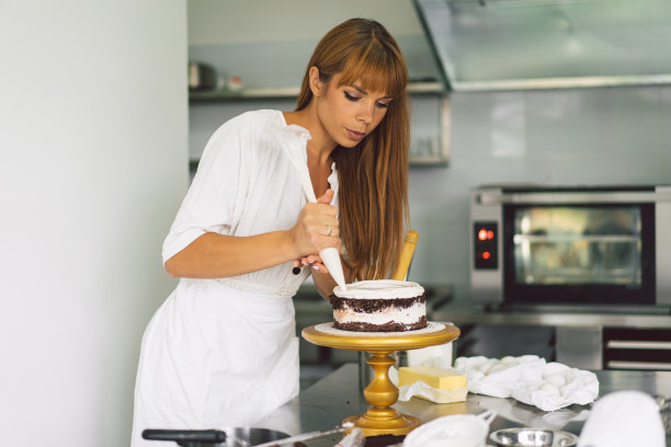 糖果商女孩正在准备一种有白奶油和巧克力的蛋糕饼干。面粉制品或甜点的概念配料。图片下载