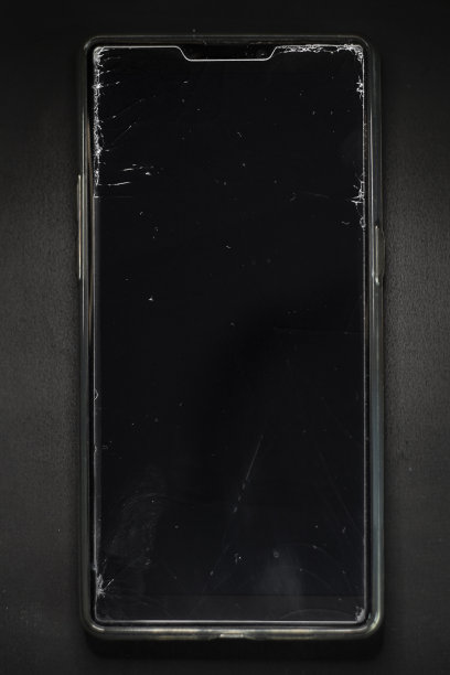 一个破碎的智能手机屏幕上的裂痕。黑暗背景下的手机保护膜损坏。照片在软焦点在高倍放大。图片下载