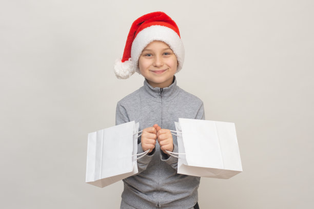一个戴着圣诞帽微笑的男孩拿着纸袋。模拟了图片下载