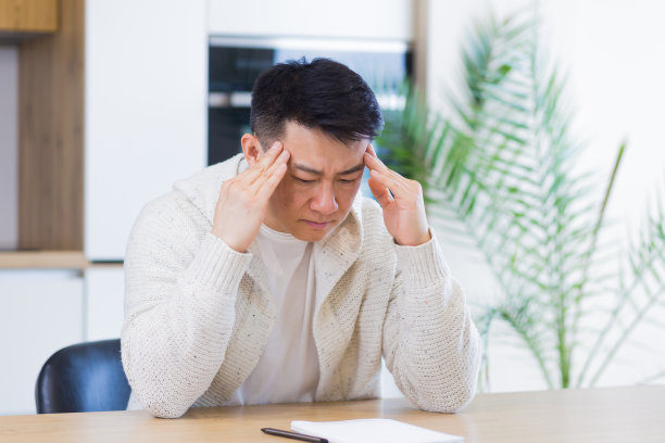 深思熟虑的严肃的年轻亚洲人看着别处。学生作家坐在家里的办公桌与笔记本电脑思考灵感，搜索解决方案，思想迷失，梦想解决财务问题图片下载