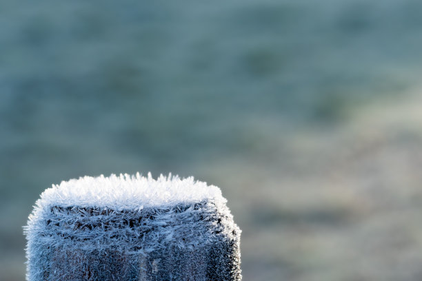 木栅栏顶上覆盖着冰晶，在晨光的照射下。霜冻冬季的概念，寒冷的温度，霜冻。微距镜头与背景模糊和复制空间。图片下载