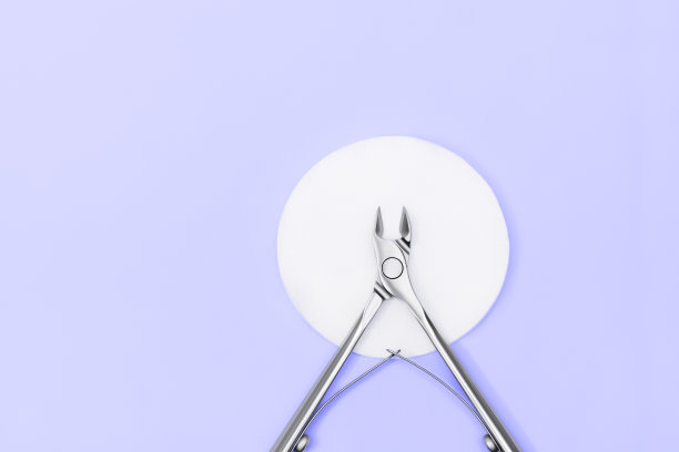 指甲剪在白色棉垫上的蓝色背景。指甲护理设备。不锈钢钳在紫色背景。图片下载
