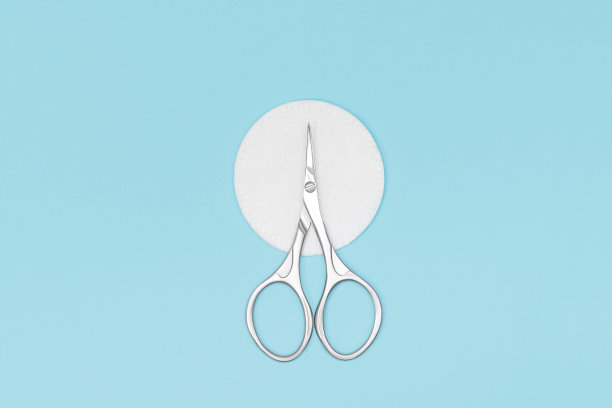 指甲剪在白色棉垫上的蓝色背景。指甲护理设备。不锈钢剪刀在蓝色的背景。图片下载