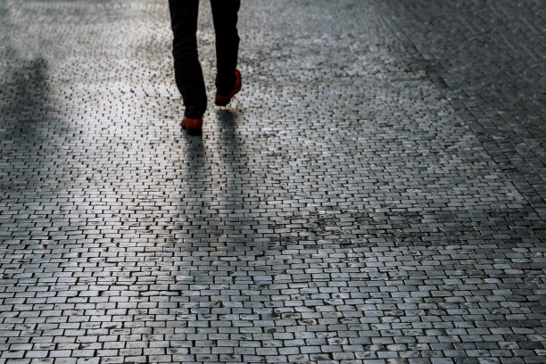 从后面看人行道的城市景观，一个男人沿着人行道走在一个稳定的照明的地方。软的焦点。图片下载