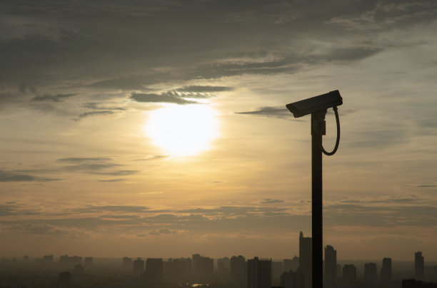 现代监控摄像机的阴影在城市景观和摩天大楼的背景下，太阳在日落前明亮地照耀着。图片下载