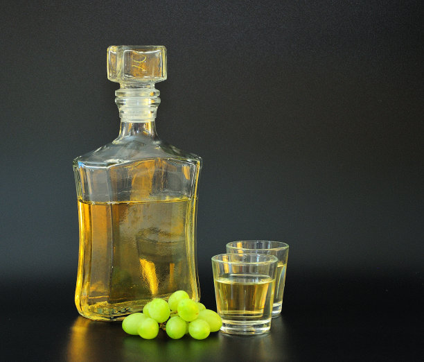 格拉巴(Grappa)是一种用玻璃瓶和黑底酒杯盛放的烈酒，旁边放着一串成熟的白葡萄。图片下载
