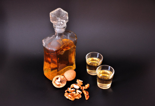 以核桃为基酒的利口酒，自制的烈酒装在两个玻璃杯和一个黑色背景的玻璃瓶里，旁边是碎坚果。图片下载