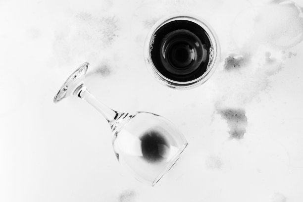 一杯红酒和一个打翻的杯子与残余的葡萄酒在白色的背景湿透和染色葡萄酒顶部视图，黑白照片图片下载
