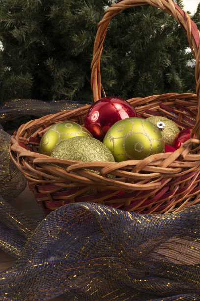 柳条篮子里有球，一些球周围有闪光的和蓝色的装饰丝带，工作室里的装饰品，背景里有一棵人造圣诞树图片下载