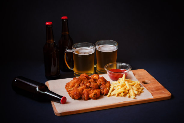 鸡翅和薯条放在砧板上，啤酒和啤酒的黑色背景。图片下载