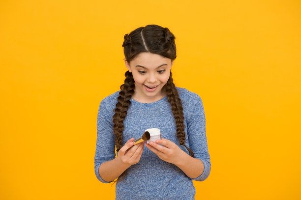 定义的美丽。女性的美丽与时尚。小女孩用化妆刷敷粉。穿上脸红。惊讶的孩子有辫子。天然儿童化妆品。快乐的小女孩创造自己的形象图片下载