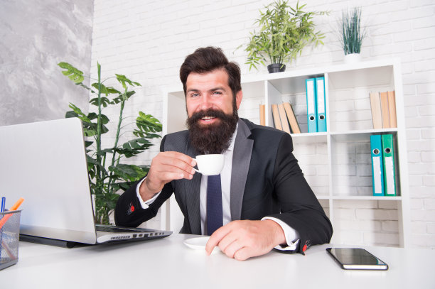接待室。尊敬的首席执行官。帅哥老板坐在办公室里喝咖啡。舒适的工作空间。留着胡子的嬉皮士正装，边喝咖啡边放松。没有上好的咖啡，办公室生活是不可想象的图片下载