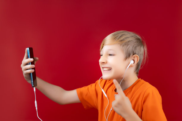 一个兴高采烈的男孩在一个红色的背景，手里拿着电话和耳机图片下载