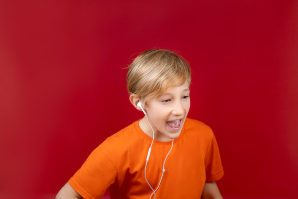 一个兴高采烈的男孩在一个红色的背景，手里拿着电话和耳机图片下载