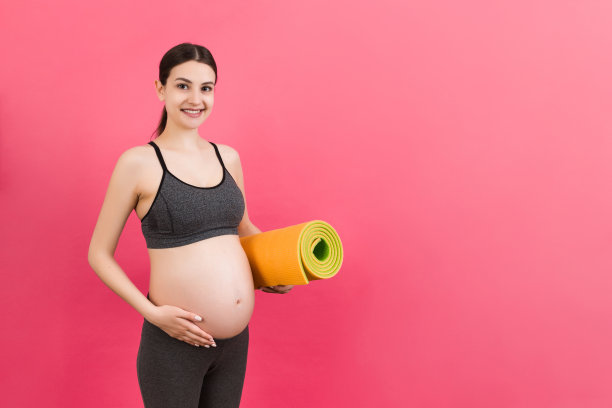 孕妇抱着瑜伽垫站在彩色背景上。工作室拍摄，设计的自由空间图片下载