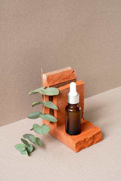 面部血清装在棕色玻璃瓶中，移液管放在碎砖台上，绿色桉树枝放在米色背景上。血清或精油广告。自然生态化妆品。垂直图图片下载