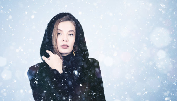 在雪的背景下，一个穿着黑色毛皮大衣的年轻女孩的画像图片下载