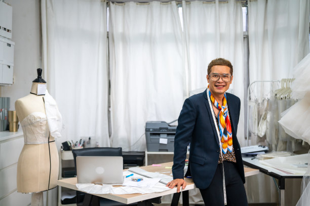 亚裔男新娘店老板在婚礼工作室制作婚纱缝纫图案的肖像。图片下载