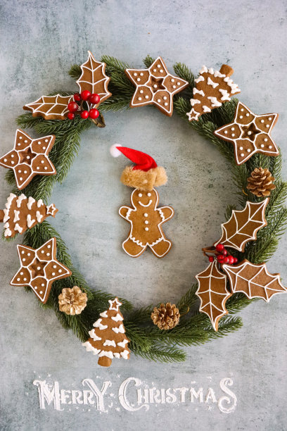近距离图像的云杉花环装饰自制，姜饼圣诞树，星星和冬青树叶子冰镇白色，皇家糖衣，松果和红色浆果，个人姜饼人戴圣诞帽在灰色的背景，圣诞快乐的信息图片下载