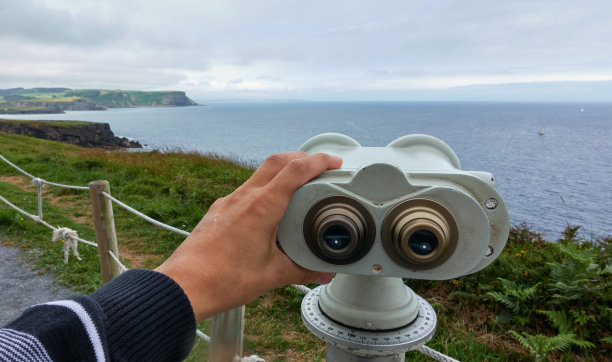 男子在多云的天气手持双筒望远镜看海岸图片下载
