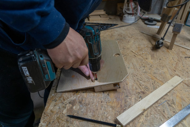 照片中，一个在车间里钻木制品的男性手。生产图片下载