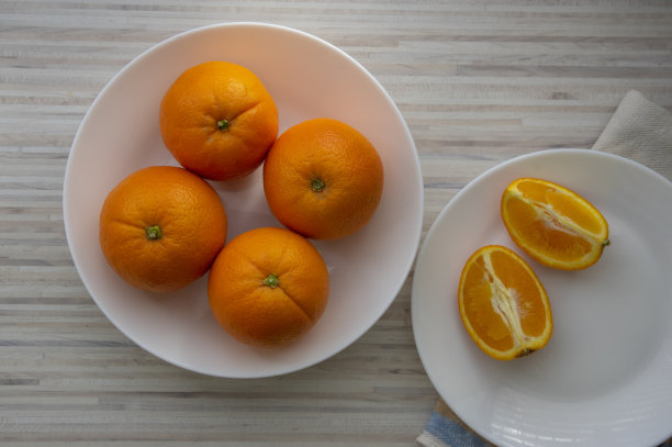 一组四颗橘子放在白色的盘子上，放在阳光下的餐桌上，生的美味健康的水果图片下载