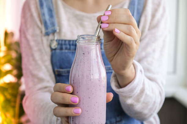 女性手捧着蓝莓奶昔。一名妇女正在喝由生蓝莓泥、香蕉、牛奶、酸奶和白软干酪制成的蛋白质奶昔图片下载