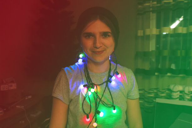 圣诞节的有趣的肖像。时髦的年轻女人庆祝圣诞节。年轻人在五颜六色的彩灯下玩寒假。裹在彩色圣诞彩灯中的女人。红色和绿色在狂欢图片下载