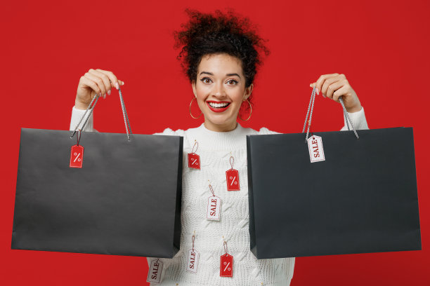 年轻的女服装师穿着白色针织毛衣与标签出售在商店的陈列室持有包袋与购买后，购物出售文字铭文孤立在纯红色的背景工作室。图片下载