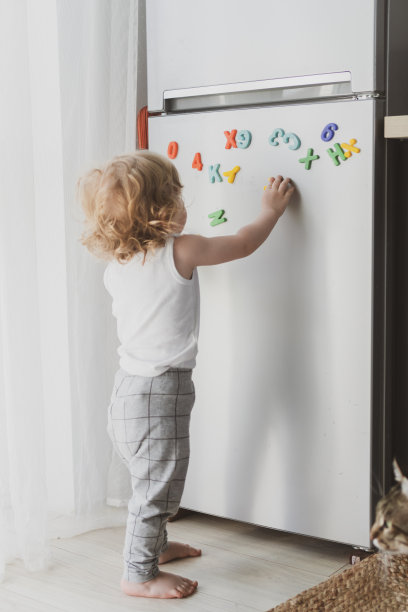 一个可爱的小孩在玩冰箱上的玩具字母图片下载