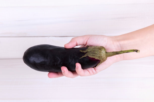 紫茄子在一个人的手上，白色的木制背景。图片下载