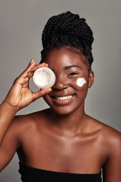 一个迷人的年轻女子在灰色背景上涂抹润肤霜的工作室镜头图片下载