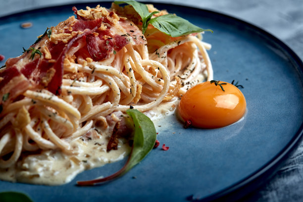 经典的加蛋黄意大利面放在盘子里。意大利面放在蓝色盘子里，背景是黑色的。意大利菜的概念，精美的上菜，特写图片下载