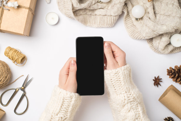 第一个人顶视图照片的手在毛衣拿智能手机在礼盒围巾圣诞树球球果八角蜡烛剪刀线轴在孤立的白色背景与copyspace图片下载