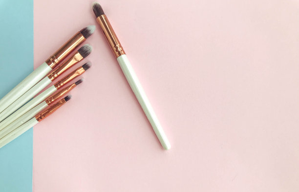 化妆刷在粉色和蓝色的背景上。一组用于在脸部应用纹理的笔刷。男女化妆。画眼线笔，口红，光泽笔，眼影的刷子图片下载