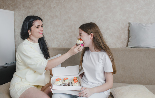 一位慈爱的母亲坐在沙发上给她的女儿吃美味的蛋糕图片下载