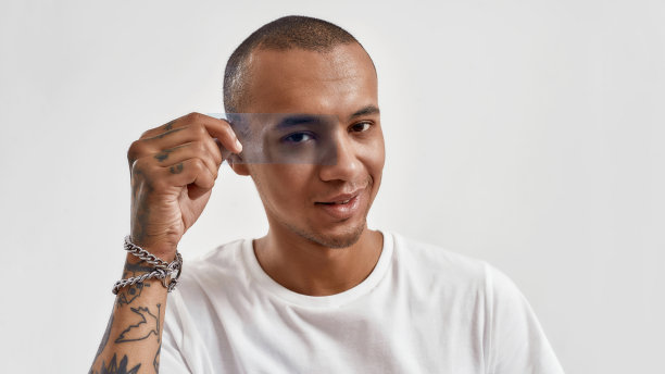 快乐的混合种族的家伙拿着蓝色的电影在他的眼睛前面，对着相机微笑，在白色的背景下孤立地摆姿势图片下载