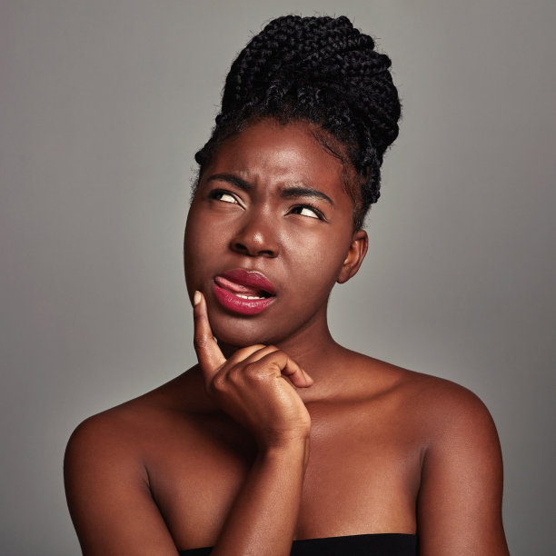 一个迷人的年轻女子在灰色背景下看起来不确定的工作室拍摄图片下载