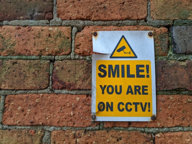 砖墙上挂着“笑一笑，你在闭路电视上”的监控标识图片下载