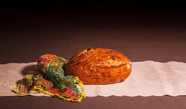 铺在白色绣花桌布上的粗糙面包。图片下载