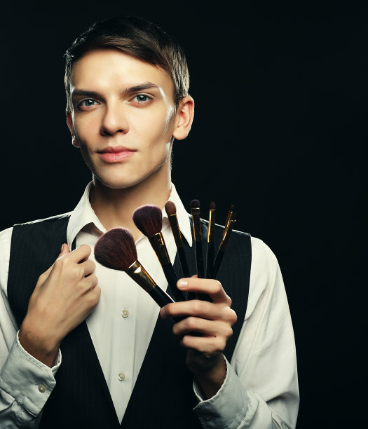 年轻的男性化妆师与化妆刷在黑暗上摆姿势图片下载