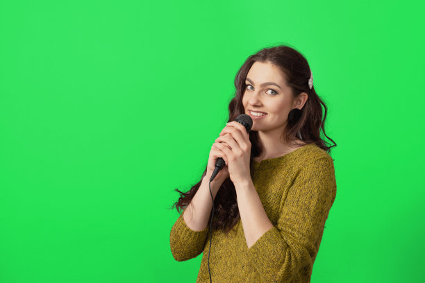 有吸引力的十几岁的女人说话与麦克风对绿色背景，会议发言人图片下载