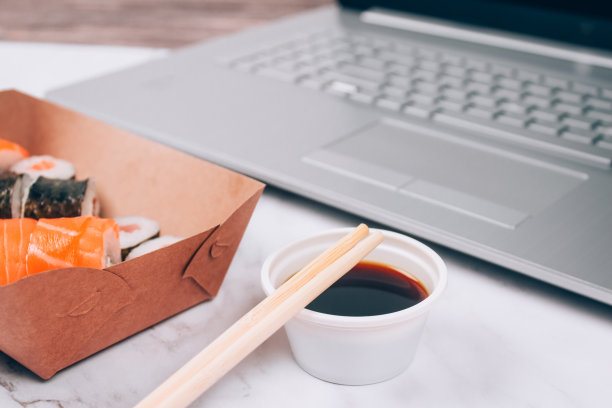 不同的寿司卷与三文鱼在送递纸盒上的白色大理石桌子背景与笔记本电脑-双卷，村卷和细卷。网上订餐和外卖的概念图片下载