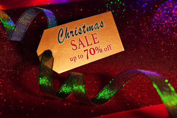 金色标签与文字-圣诞销售高达70折，与明亮的绿色丝带，明亮的节日豪华闪亮的红色背景。图片下载